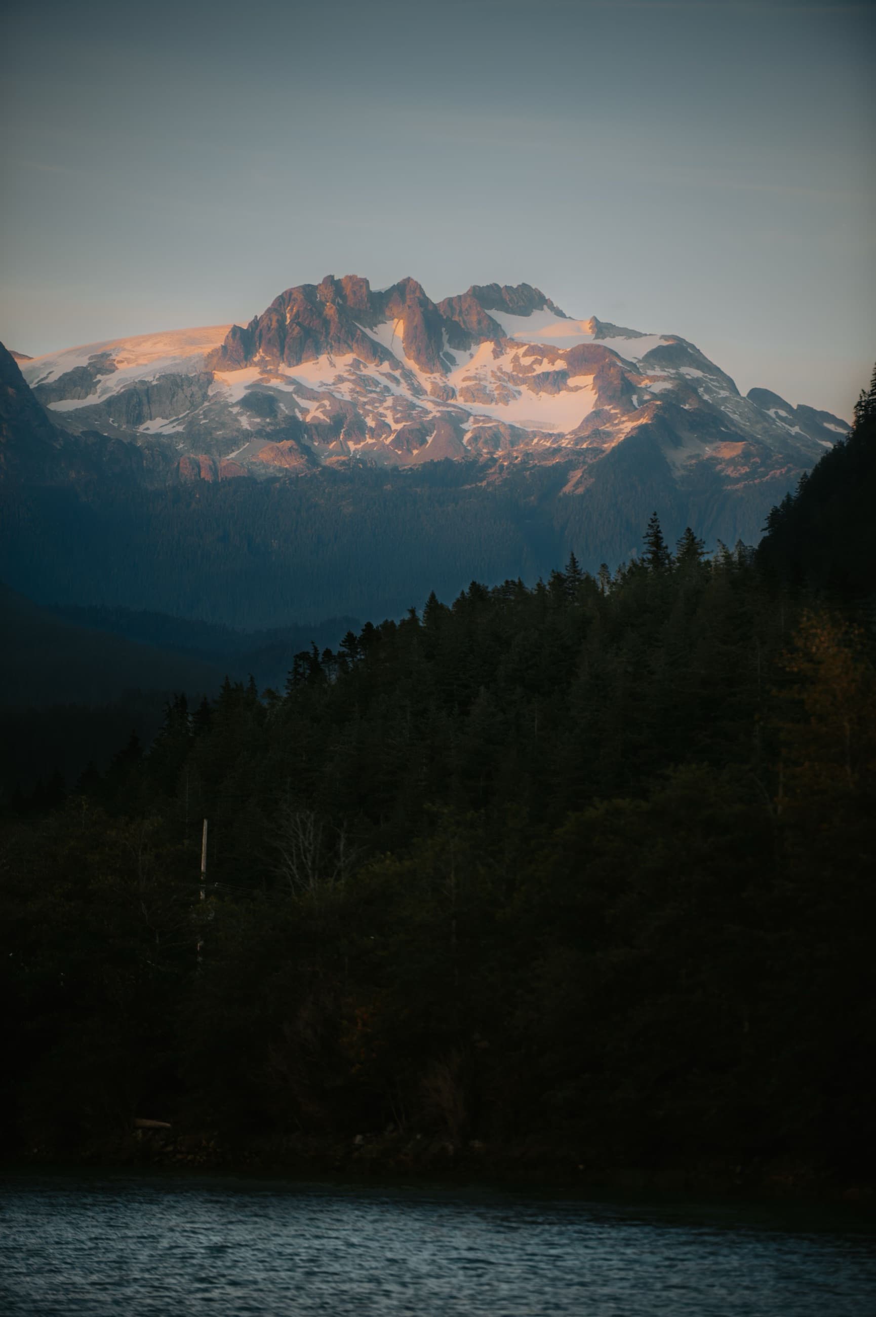 A snow-capped Coast Mountain peak glowing at sunset above a forested Squamish valley